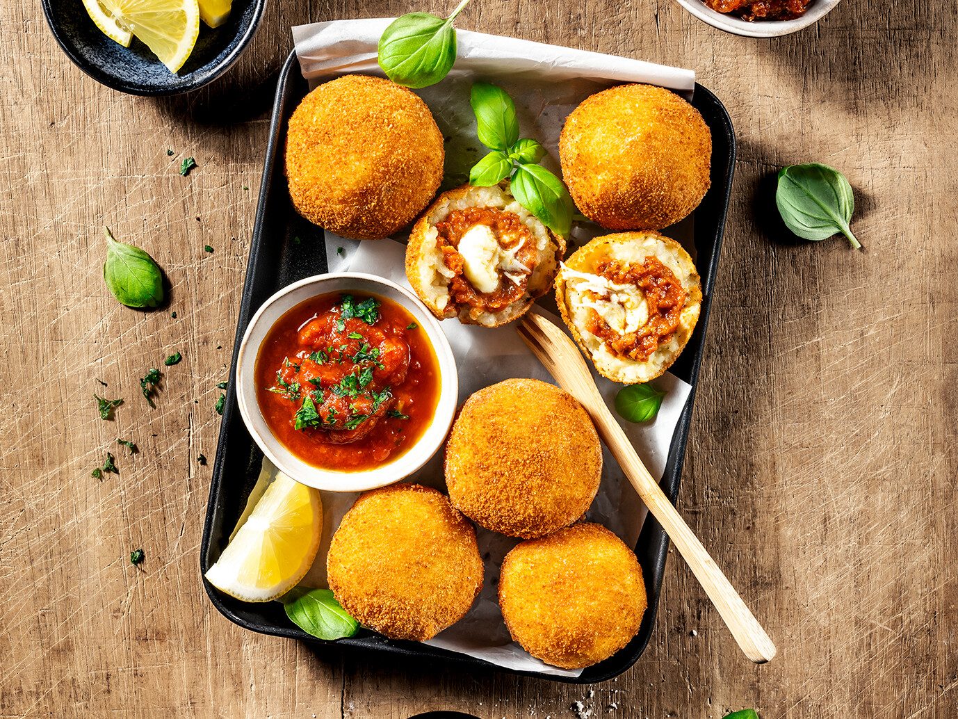 Arancini: Frittierte Reisbällchen aus Sizilien Ein Teller mit frittierten Reisbällchen, Saucen und Zitronen.